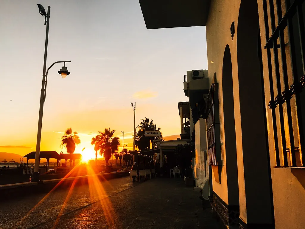Paseo marítimo de Pedregalejo al atardecer, con el sol bajando entre las palmeras